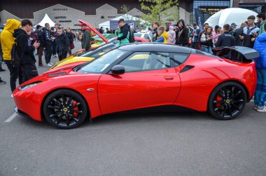 Çarpıcı kırmızı Lotus Evora spor arabası açık havada sergileniyor, özel ön ızgarası, parlak farları ve siyah bir çatısı var.