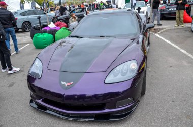 Eşsiz özelleştirilmiş Chevrolet Corvette C6, açık hava otomobil etkinliğinde kaputunda mat siyah yarış çizgisi ile koyu metalik mor boya ile sergilenmektedir.
