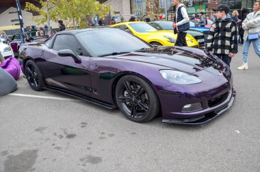Eşsiz özelleştirilmiş Chevrolet Corvette C6, açık hava otomobil etkinliğinde kaputunda mat siyah yarış çizgisi ile koyu metalik mor boya ile sergilenmektedir.