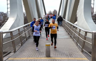 Bir grup koşucu gündüz yarışı sırasında şık şehir köprüsünden geçiyor. Katılımcılar atletizm kıyafeti, takım çalışması, dayanıklılık ve açık hava spor etkinliği giyiyorlar.