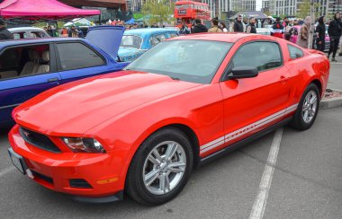 Canlı kırmızı Ford Mustang coupe klasik Amerikan midilli arabasıdır. Çok dilli alaşımlı tekerlekleri vardır. Sportif ve kaslı bir varlığa sahiptir.