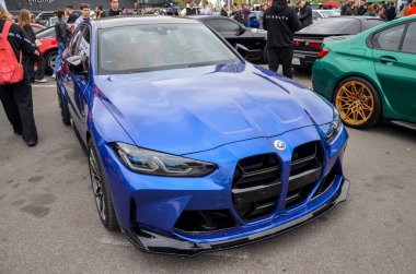 Çarpıcı mavi BMW M3 G80 performans sedan, agresif stile sahip, tartışmalı geniş böbrek ızgarası, parlak farlar, ve siyah çatı