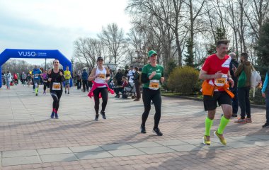Koşucular kalabalık bir açık hava yarışını mavi şişirilebilir kemerin altında başlatırken, izleyiciler yolu çiziyor.