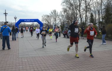 Koşucular kalabalık bir açık hava yarışını mavi şişirilebilir kemerin altında başlatırken, izleyiciler yolu çiziyor.