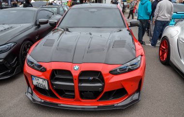 Canlı kırmızı BMW M3 G80, yüksek performanslı lüks bir spor sedan karbon fiber kapüşonlu ve önde öne çıkan bir ayrıştırıcı, sportif karakterini vurguluyor.