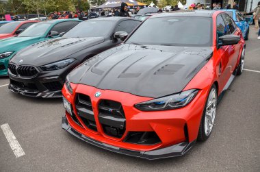 Canlı kırmızı BMW M3 G80, yüksek performanslı lüks bir spor sedan karbon fiber kapüşonlu ve önde öne çıkan bir ayrıştırıcı, sportif karakterini vurguluyor.