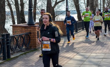 Gülümseyen kadın koşucu, güneşli ve serin bir hava ortamında açık hava yarışında bir gruba liderlik ediyor.