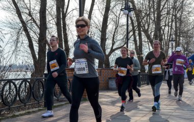 Gülümseyen kadın koşucu, güneşli ve serin bir hava ortamında açık hava yarışında bir gruba liderlik ediyor.
