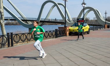 Parlak atletizm kıyafetleri içinde iki genç kız arka planda modern köprü ile rıhtım boyunca koşuyorlar enerji yarışması ve aile dostu spor gösterileri yapıyorlar.