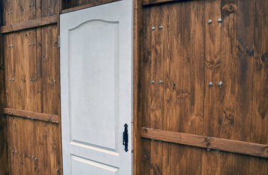 Beyaz, kavisli üst kapı sıcak kahverengi ahşap bir duvara kurulmuş. Ahşap duvarların yatay destek kirişleri ve görünür gümüş vidaları var. Kapının siyah bir kolu var.