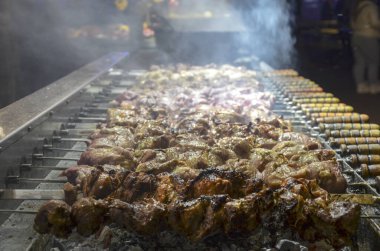 Sıcak kömürlerin üzerinde pişen et şişleri çok dumanla sonuçlanıyor. Etler ön planda iyice kömürleşmiş olandan arka planda pişmiş olana kadar değişiyor.