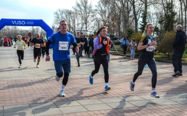 Bir grup koşucu açık hava yarışında parlak mavi şişme kemer altında yarışıyor. Seyirciler kurs boyunca tezahürat yapıyor, fitness, takım çalışması ve toplum ruhu sergiliyor