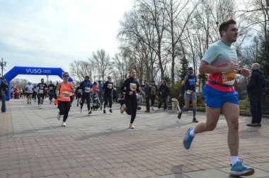Bir grup koşucu açık hava yarışında parlak mavi şişme kemer altında yarışıyor. Seyirciler kurs boyunca tezahürat yapıyor, fitness, takım çalışması ve toplum ruhu sergiliyor