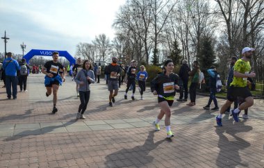 Bir grup koşucu açık hava yarışında parlak mavi şişme kemer altında yarışıyor. Seyirciler kurs boyunca tezahürat yapıyor, fitness, takım çalışması ve toplum ruhu sergiliyor