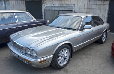 Klasik gümüş rengi Jaguar XJ lüks sedan, zamansız İngiliz tasarımı ve zarif oranlarıyla geleneksel lüks ve otomotiv prestijini temsil ediyor.