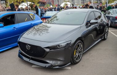 Gösterişli koyu gri Mazda 3 hatchback 4. nesil, özel çoklu konuşmalı alaşımlı tekerlekler parlak sarı fren kalibreli ve sportif düşük duruşu var.