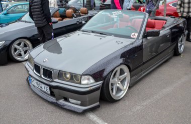 Yoğun özelleştirilmiş koyu gri BMW E36 üstü açık, çarpıcı bir şekilde indirgenmiş duruş, geniş gövdeli çamurluklar ve cilalanmış derin pazar sonrası tekerlekleri var.