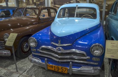 İki ton mavi GAZ-M20 Pobeda sedan, ikonik bir Sovyet dönemi arabası, kendine özgü ponton tarzı kaportası, büyük krom ızgara ve yuvarlak lambalar sergiliyor.