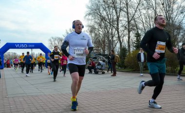 Canlı koşucular bir park sokak yarışında yarışır, mavi şişirilebilir kemerin altından geçerken izleyiciler toplum fitness ve enerjisini iletirler.