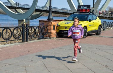 Genç bir kız nehir kıyısındaki bir yürüyüş yolu boyunca koşar açık hava spor salonu ve hayat dolu bir sokak hayatı sergiler.