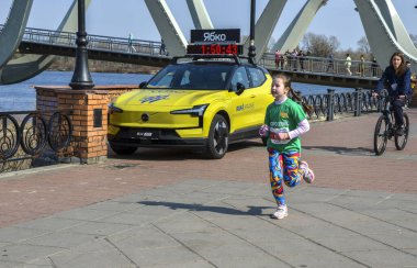 Genç bir kız nehir kıyısındaki bir yürüyüş yolu boyunca koşar açık hava spor salonu ve hayat dolu bir sokak hayatı sergiler.