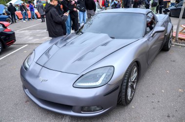 Gösterişli, gri Chevrolet Corvette C6 jenerasyon spor arabası. Özel bir kaputu ve açık hava araba fuarına park edilmiş ince bir duruşu var.