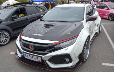 Son derece modifiye edilmiş, geniş gövdeli siyah kapüşonlu beyaz Honda Civic sedan açık hava araba fuarında sergileniyor.