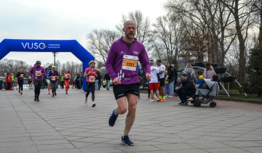 Erkek koşucu, seyirciler izlerken mavi bir kemer tarafından çerçevelenmiş açık hava parkındaki bitiş çizgisine doğru itiyor.