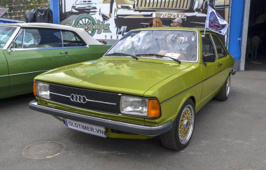 İyi korunmuş kireç yeşili 1978 Audi 80 B1 nesil sedan, özel altın ağ tekerlekleri, açık havada klasik bir araba fuarında park edilmiş.