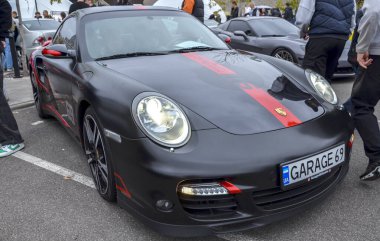 Güçlü mat siyah Porsche 911 GT2 spor coupe, çarpıcı kırmızı yarış şeritleri ve aksanları, açık hava araba fuarında park