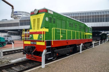 Yeşil, sarı ve kırmızı Sovyet döneminden kalma dizel lokomotif ChME2-333, arka planda modern istasyon mimarisi ile tuğla platformun yanına park edilmiştir.