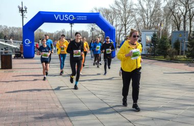 Renkli giyimli koşucular finişe doğru koşuyor. Açık hava parkında, izleyicilerin ve bahar güneşinin olduğu büyük mavi şişme kemerin altında.
