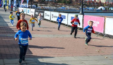 Suyun kenarındaki tuğladan bir güvertede yarışan genç çocukların canlı sahnesi. Enerjik, eğlenceli bir an. Takım çalışması, fitness ve dostça bir rekabet.