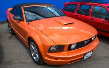 Parlak turuncu beşinci nesil Ford Mustang klasik Amerikan midilli arabası retro fütüristik tasarım çift farları ve koşu atı amblemi ile öne çıkan ön ızgarası.