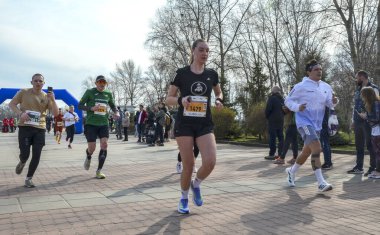 Koşucular bir şehir parkı yarışında finişe doğru koşuyorlar. Dinamik açık hava sahnesi fitness, rekabet ve toplumsal desteği vurguluyor