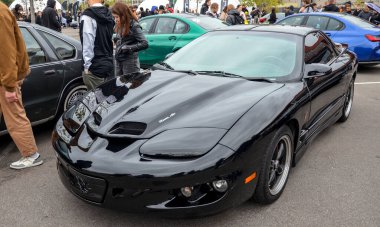 Glossy black Pontiac Firebird Trans Am sports coupe, featuring its distinctive hidden headlights, low slung aerodynamic design, and performance hood with air scoops