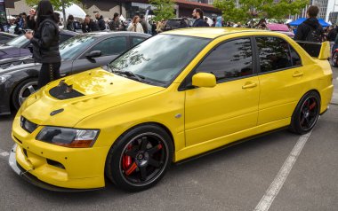 Çarpıcı, saldırganca modifiye edilmiş sarı Mitsubishi Lancer Evolution IX performans sedan, havalandırma kaputu, geniş ön ayırıcı ve kara borsa tekerlekleri var.
