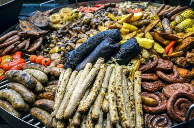 Büyük, yuvarlak ızgara çeşitli ızgara sosisler, kanlı sosisler, patatesler, soğanlar ve kırmızı biberlerle dolu.