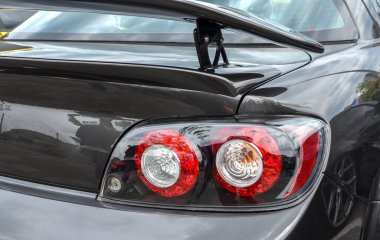 Koyu gri Mazda RX-8 bir arabanın arkasında parlak bir spoiler ve açık merkezli çift dairesel kırmızı stop lambaları bulunur.