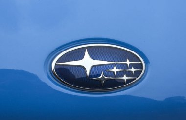 Mavi bir arka planda altı adet dört köşeli yıldızın yer aldığı gümüş Subaru amblemi, canlı mavi bir araba kaputu üzerine kuruludur.