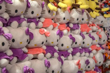 Hello Kitty pelüşlerinden oluşan duvar üst üste dizilmiş duruyor. Beyaz karakterler çeşitli mor ve pembe elbiseler ve fiyonklar giyer.