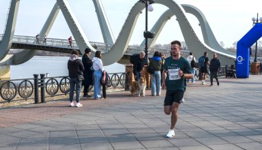 Organize bir maraton etkinliği sırasında nehir kenarındaki bir gezinti alanında yarışan rekabetçi erkek koşucu. Enerjik açık hava fitness ve şehir sporları sahnesi