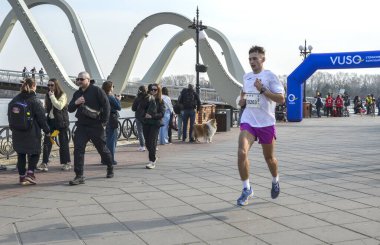 Organize bir maraton etkinliği sırasında nehir kenarındaki bir gezinti alanında yarışan rekabetçi erkek koşucu. Enerjik açık hava fitness ve şehir sporları sahnesi