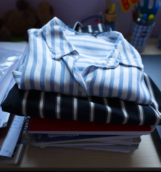 Clothes, teenage winter folded shirts, student in his bedroom with books underneath, natural lighting from the window.