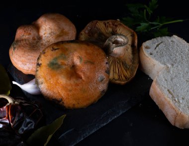 Sarımsak ve defne yaprağıyla pişirilmesi gereken Niscalos mantarları, siyah arka plan ve dokuları ön plana çıkaran sert ışıklandırma..