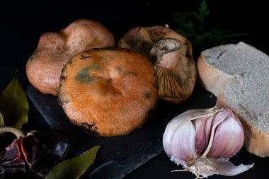 Sarımsak ve defne yaprağıyla pişirilmesi gereken Niscalos mantarları, siyah arka plan ve dokuları ön plana çıkaran sert ışıklandırma..