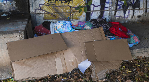 Social problem, sad homeless man sleeping in the street under a bridge covered with cardboard outdoors in cold winter day.