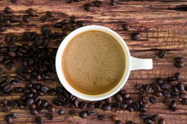 Eski ahşap üzerine kavrulmuş kahve çekirdekleri ile beyaz kahve fincanı.