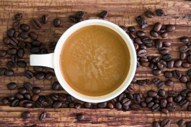 Eski ahşap üzerine kavrulmuş kahve çekirdekleri ile beyaz kahve fincanı.