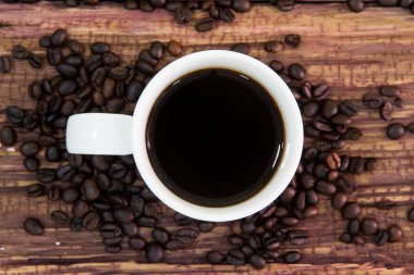 Eski ahşap üzerine kavrulmuş kahve çekirdekleri ile beyaz kahve fincanı.